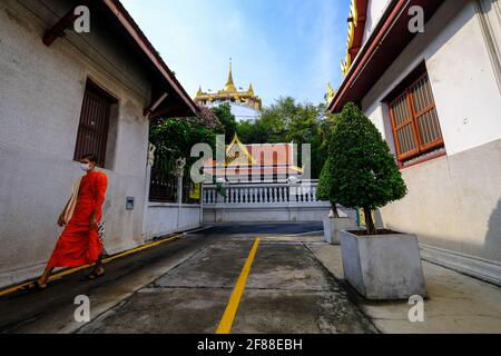 A young Thai buddhist monk walks along a road beneath Wat Saket (Golden Mount Temple) in Bangkok, Thailand Stock Photo