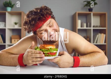 Chubby obese caucasian man in sportswear holding burger on plate portrait Stock Photo