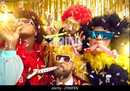 Multiethnic friends company in carnival wear blowing in party pipes having fun Stock Photo