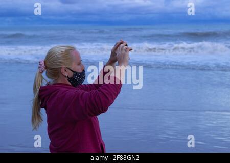 Woman with face mask on the beach on a cloudy day. Stock Photo
