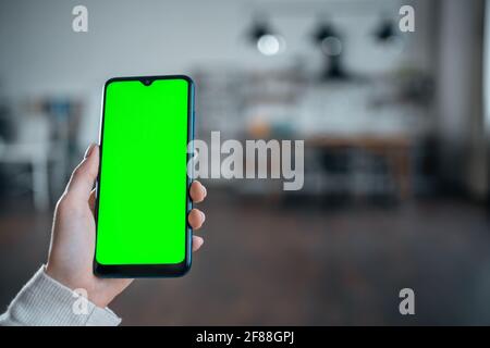 closeup of female hand using smartphone with green screen mockup at home kitchen Stock Photo