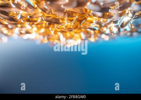 handful of golden fish oil capsules omega 3 vitamins on blue background Stock Photo