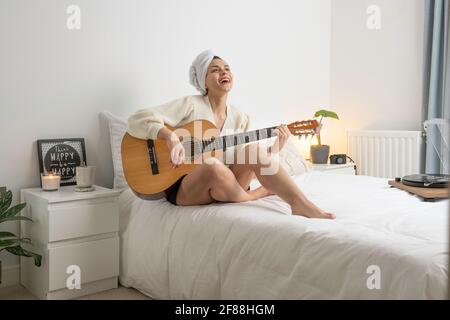 woman playing guitar on her room with a towel on her head Stock Photo