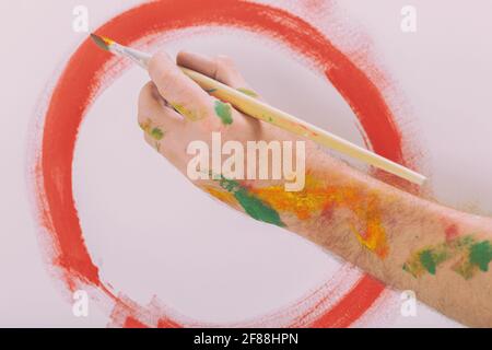 Painter's hand holding paintbrush and painting on canvas Stock Photo