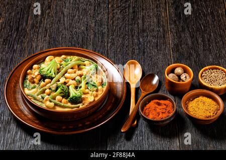 vegetarian coconut curry with chickpea, green beans, cauliflower and broccoli florets in a rustic bowl on a dark wooden table with spices, indian cuis Stock Photo