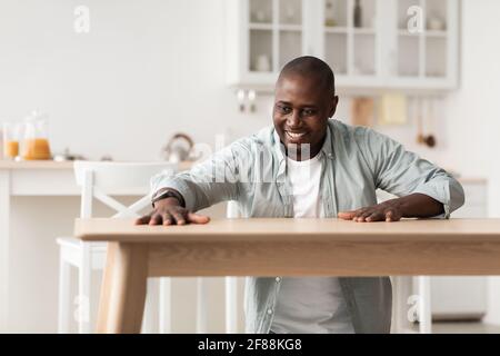 Happy african american man touching new wooden table, feeling pleasure of installing desk by yourself Stock Photo