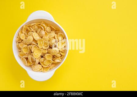 corn flake in bowl and empty space for text isolated on yellow background, plate of cornflakes, healthy breakfast concept, top view Stock Photo