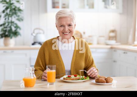 Attractive grandmother having lunch in kitchen alone Stock Photo