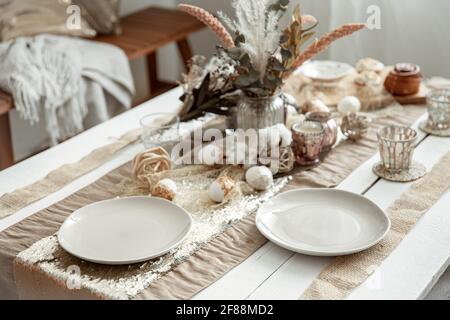 Empty plates and glasses on a decorated dining table for the Easter holiday. Beautiful hygge-style table setting. Stock Photo