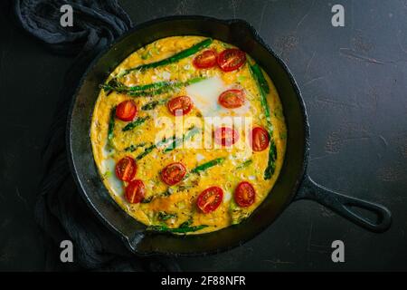 Delicious fritatta with green asparagus and cherry tomatoes in pan Stock Photo