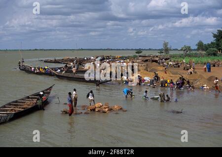 Village with women washing on shore River Niger, and men transporting stones in pirogue, Ségou, Mali Stock Photo
