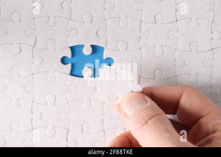 Man inserting last piece into white puzzle closeup Stock Photo