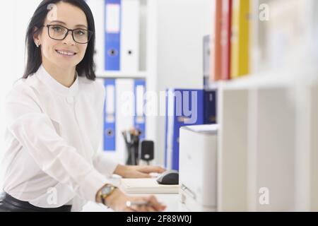 Young woman with glasses sitting at table in office Stock Photo