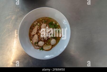 Thai spicy noodle soup with pork and fish balls in white ceramic bowl. Top view, Copy space, Selective focus. Stock Photo