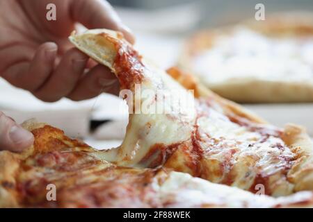 Man tearing off piece of delicious pizza with his hand closeup Stock Photo