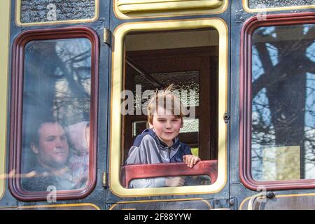 Bewdley, UK. 12th April, 2021. It's full steam ahead on the Severn Valley Railway as this ever-popular heritage railway reopens following the easing of lockdown restrictions today. The family captured here on board the passing 'Adventurer' service are returning home to Bridgnorth after a fabulous day riding the rails, enjoying the afternoon sunshine. Credit: Lee Hudson/Alamy Live News Stock Photo