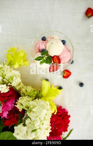Tasty Ice cream and fresh blueberries, strawberry in the bowl, presented with flower on a table in a garden during summer season for a party Stock Photo