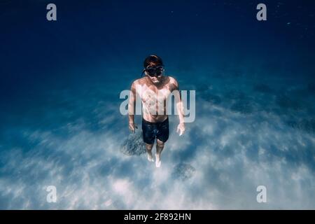 Freediver in red swimsuit with fins posing underwater over sand in tropical ocean. Stock Photo