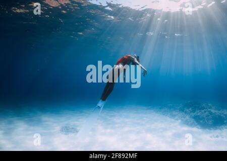 Woman freediver in swimsuit with fins glides underwater over sand in tropical ocean. Stock Photo