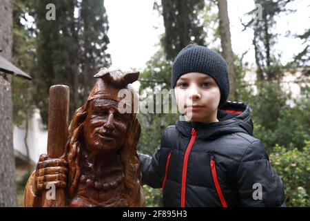 Boy with wooden sculpture of Baba Yaga in Gurzuf Park in spring Stock Photo