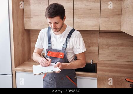 Plumber in uniform signs a contract for services in the kitchen Stock Photo