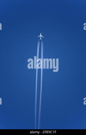 Airplane with contrails in clear blue sky, Cruising altitude. Jets leave white trails, or contrails, in their wakes for the same reason you can someti Stock Photo