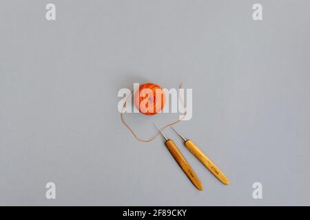 Set for needlework, knitting - two crochet hooks and round ball of orange thread on gray background. Top view. Copy space. Selective focus. Stock Photo