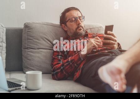 Laid back barefoot casual man taking a break on mobile smart phone while working from home, selective focus Stock Photo
