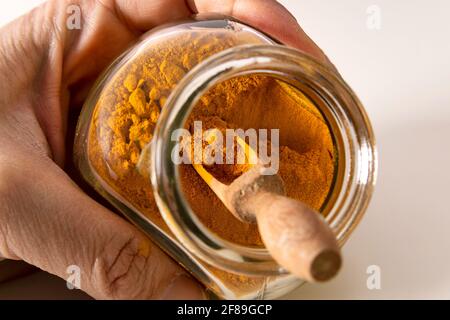 Close up of hand holding glass jar with curry spice powder and wooden spoon. Stock Photo