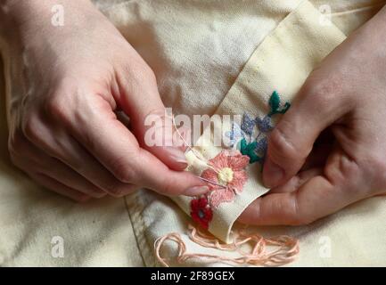 Embroidery in woman hands, female doing flower pattern embroidery on grandma natural clothes, closeup, cottagecore living, eco lifestyle, slow simple Stock Photo