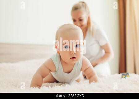 Mother's day. Young happy mother playing with her newborn baby son at home. Family having fun lying on bed in bedroom. Stock Photo