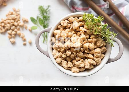 Closeup view of a white casserole full of raw chunks of soya meat. An aromatic twig is at the top. Stock Photo