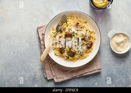 Dining italian pasta risoni, mushrooms, sauce, Parmesan, thyme, garlic, olive oil, in white plate over slate, stone or concrete background. Top view w Stock Photo