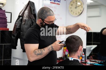 A hairdresser wearing a face mask cuts hair of a client during the reopening. Shops, restaurants, bars and other businesses reopened today after almost four months as further lockdown rules are relaxed in England. Stock Photo