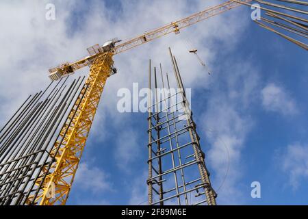 Tower construction crane and reinforcements steel bars against the blue sky. Big yellow construction crane. Close up steel construction armature. Stock Photo