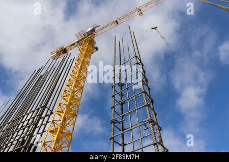 Tower construction crane and reinforcements steel bars against the blue sky. Big yellow construction crane. Close up steel construction armature. Stock Photo