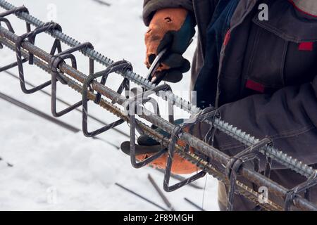 Concrete reinforcement. Tool at a construction site. The construction tool for monolithic works. Workers hands using steel wire and pincers to secure Stock Photo