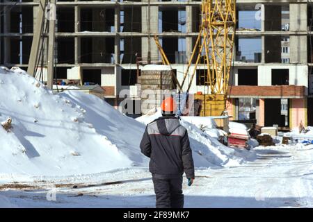 A builder in uniform and an orange construction helmet goes to a construction site in winter Stock Photo