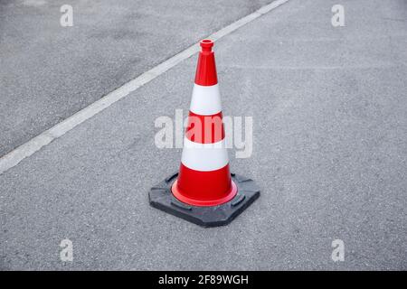 single red and white striped warning cone on gray asphalt, by day without people Stock Photo