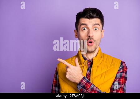 Photo of funny impressed young guy dressed yellow vest pointing one finger empty space isolated purple color background Stock Photo