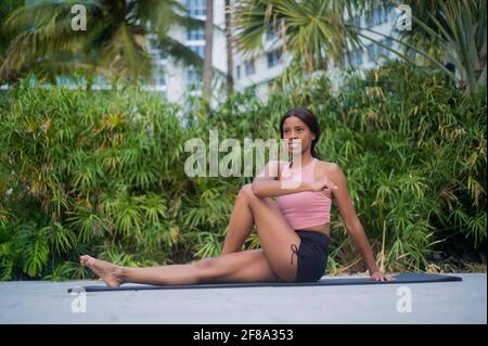 Portrait of a Young African American Woman Stretching in Yoga Pose outside during the day with tropical green background Stock Photo
