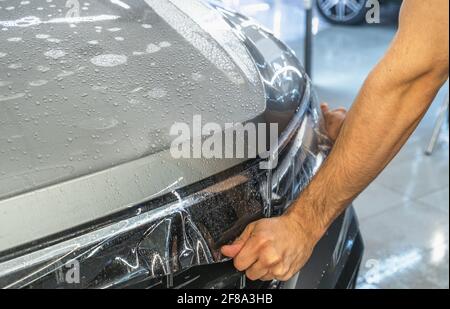 Car protection film or PPF process of wrapping and installing on car hood by detailer worker hands, close up. Stock Photo