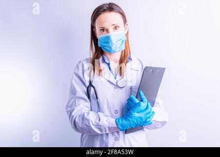 Caucasian young woman with stethoscope gown gloves and mask holding reports looking in front point medical medicine concept Stock Photo