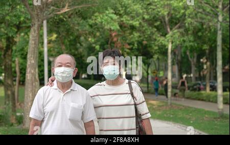 Senior Asian couple wearing face mask walking in a green park. Stock Photo