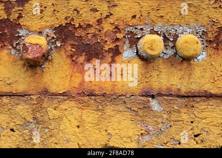 Close-up Abstract Textured Background of Three Bolts in Rusty Yellow Metal Surface with Peeling Paint Stock Photo