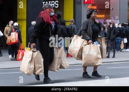 London, UK. 12th Apr, 2021. Photo taken on April 12, 2021 shows people walking with shopping bags on Oxford Street in London, Britain. In England, all shops are reopening from Monday along with hairdressers, beauty salons and other close-contact services. Restaurants and pubs are allowed to serve food and alcohol to customers sitting outdoors. Meanwhile, gyms, spas, zoos, theme parks, libraries and community centers can all open. Credit: Ray Tang/Xinhua/Alamy Live News