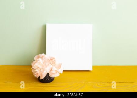 Blank white canvas with carnation flowers on wooden table. green background Stock Photo