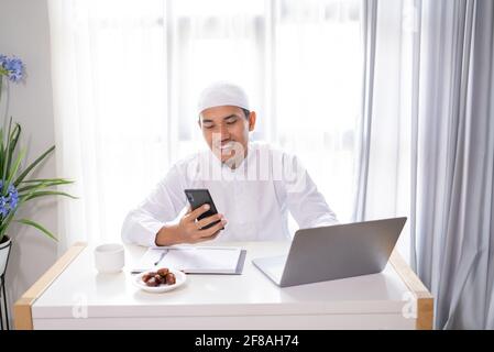 muslim businessman using his smartphone and laptop working from home Stock Photo