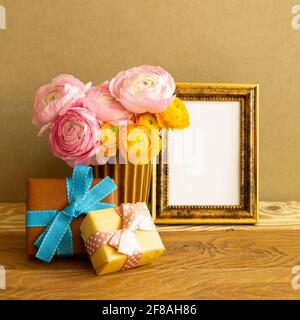 Empty photo frame with gift boxes and flowers on wooden table. brown background Stock Photo