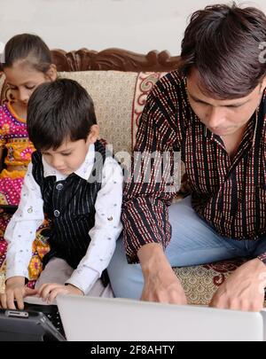 Indian family using various technologies while sitting on sofa at home Stock Photo